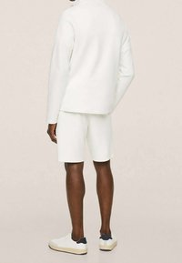 Completo atletico bianco composto da una maglietta a maniche lunghe e pantaloncini, abbinato a sneaker bianche con un accento blu navale sul tallone.