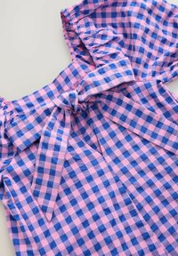 Karomuster-Oberteil in Rosa und Blau, mit einer Schleifendetail vorne und Rüschensäumen. Hergestellt aus leichtem Stoff.