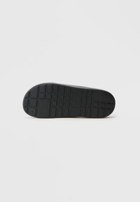 Black rubber shoe sole with textured tread pattern, featuring rectangular and square indentations for grip and traction.