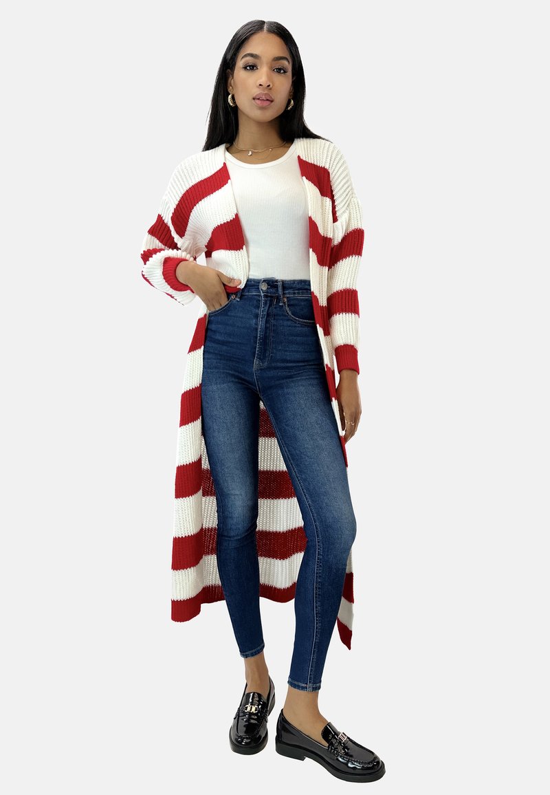Cardigán largo a rayas blancas y rojas, con textura acanalada y frente abierto. Combinado con jeans de tiro alto en azul oscuro y mocasines de charol negros.