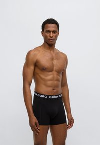 Černé boxerky s širokým černým pasem s bílým logem "BJÖRN BORG". Hladký materiál, přiléhavý střih a délka do poloviny stehna.