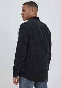 Navy corduroy shirt with a collar, long sleeves, and buttoned cuffs. Features textured fabric and a rounded hem, showing a back view.