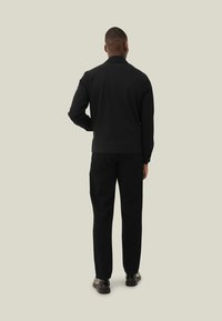 Top nero a maniche lunghe con colletto, abbinato a pantaloni neri. Il tessuto sembra liscio, con un design aderente e senza loghi o motivi visibili.