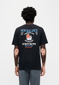 Μαύρο βαμβακερό κοντομάνικο μπλουζάκι με γραφικό σχέδιο που απεικονίζει έναν αστακό και το κείμενο «NEW BALANCE LOBSTER ROLL BAR» σε μπλε και λευκό. Κοντά μανίκια.