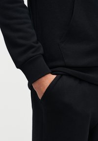 Μαύρο φούτερ με τσέπη καγκουρό και ριμπ μανσέτες, διαθέτοντας απαλή υφή και εφαρμοστό σχέδιο.