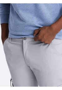 Grijze katoenen broek met een gladde textuur en een slim fit. Voorzien van een knoopsluiting en zijzakken, gecombineerd met een lichtblauwe trui.