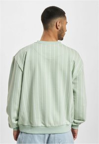 Green sweatshirt with white vertical stripes, ribbed cuff and hem, crew neck design, made of soft fabric, featuring a relaxed fit.