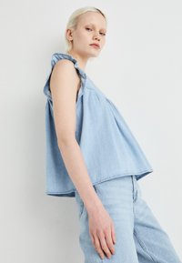 Svetlo modra denim majica z nabranimi dolgimi rokavi, ohlapen kroj in zložen dizajn. Ujemajoča svetlo modra denim hlače za usklajen videz.