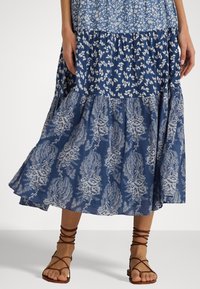 Blå lagerdress med blommönster, som har olika tryck i ljusare och mörkare nyanser. Bruna sandaler med remmar kompletterar utseendet.