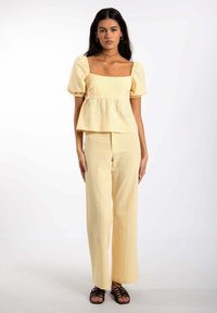 Top peplum de cuadros vichy amarillos con mangas abullonadas, combinado con pantalones de pierna ancha a juego. Tela suave y ligera con un ajuste relajado.
