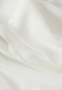 Gros plan sur un tissu tricoté côtelé blanc doux formant des plis délicats et une texture lisse.