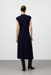 Lungo vestito blu navy con maniche a cappuccio, scollatura alta e vestibilità morbida, abbinato a stivali neri dalla punta appuntita. Tessuto a maglia liscia.