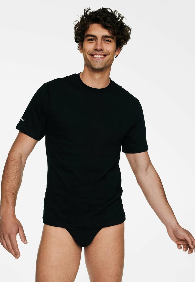 Czarna bawełniana koszulka z krótkim rękawem, o okrągłym dekolcie, noszona przez męski model, w zestawie z czarnymi strojami kąpielowymi. Gładka faktura, prosty styl.