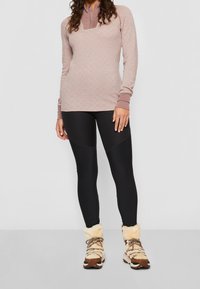 Långärmad rosa mönstrad topp med dragkedja i halsen, matchad med svarta leggings och bruna foderstövlar med beige accenter.