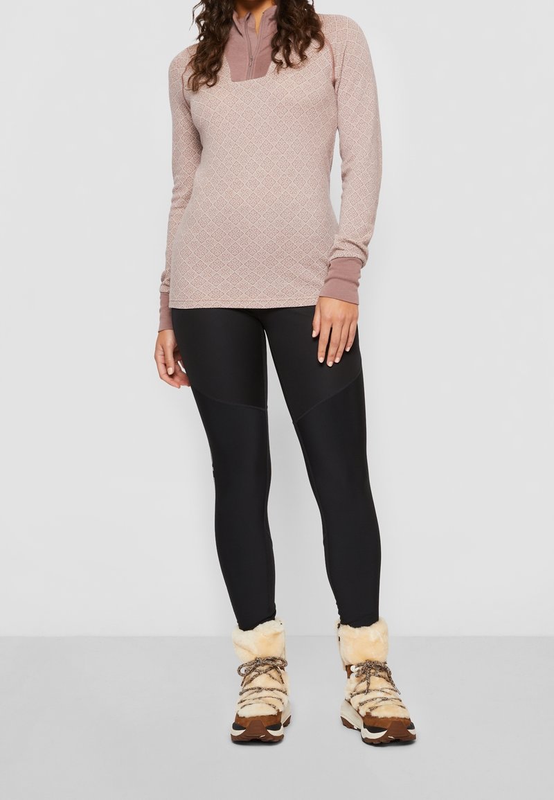 Långärmad rosa mönstrad topp med dragkedja i halsen, matchad med svarta leggings och bruna foderstövlar med beige accenter.