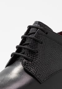 Černá kožená bota s texturovaným, šupinatým svrškem, černými šněrovadly a lesklým povrchem. Výrazná pro svůj elegantní design a kontrastní materiály.
