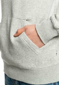 Sudadera gris de algodón con capucha, bolsillo tipo canguro, puños y dobladillo acanalados, con una superficie de tela texturizada. Diseño casual para el uso diario.