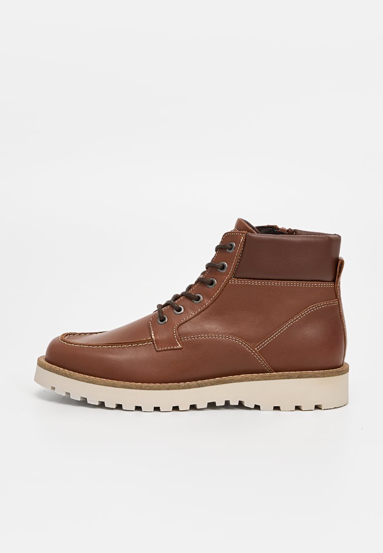 Bottines en cuir marron avec un bout arrondi, des coutures contrastées et six œillets. Semelle en caoutchouc avec un motif texturé.