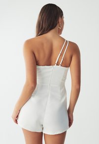 White sleeveless romper with fitted bodice, adjustable straps, and back zipper. Soft fabric, smooth texture, and short shorts design.