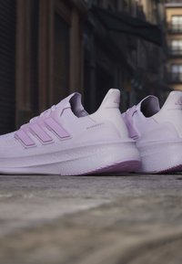 Двойка светлолилави бягащи обувки Adidas Ultraboost, почиващи на каменна повърхност в градска обстановка на открито.