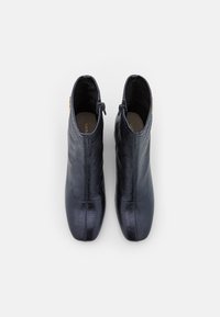 Botines de ante azul marino en cuero texturizado, con un diseño elegante, cierre lateral con cremallera y un sutil acento dorado. Punta suave y redondeada.