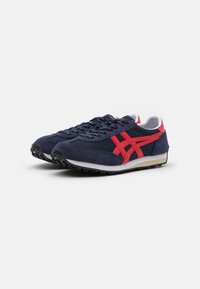 Sneakers blu navy con accenti rossi, dotati di tomaia in mesh e camoscio, lacci piatti e una suola in gomma testurizzata per una maggiore aderenza.