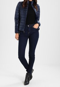 Marinblå pufferjacka med en figurnära design, ribbat svart linne under, och mörka skinny jeans, tillsammans med svarta ankelboots.