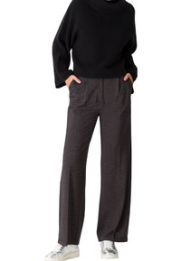 Pull noir à côtes avec un col montant, associé �à un pantalon large gris foncé avec des plis, et des baskets argentées.