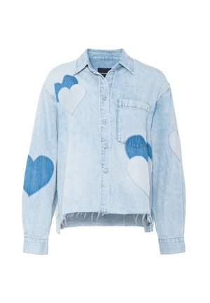 Vaaleansininen farkkutakki, jossa on sinisiä ja valkoisia sydänmerkkipaloja ja rispaantunut helma. Takissa on rintatasku ja kaulus.