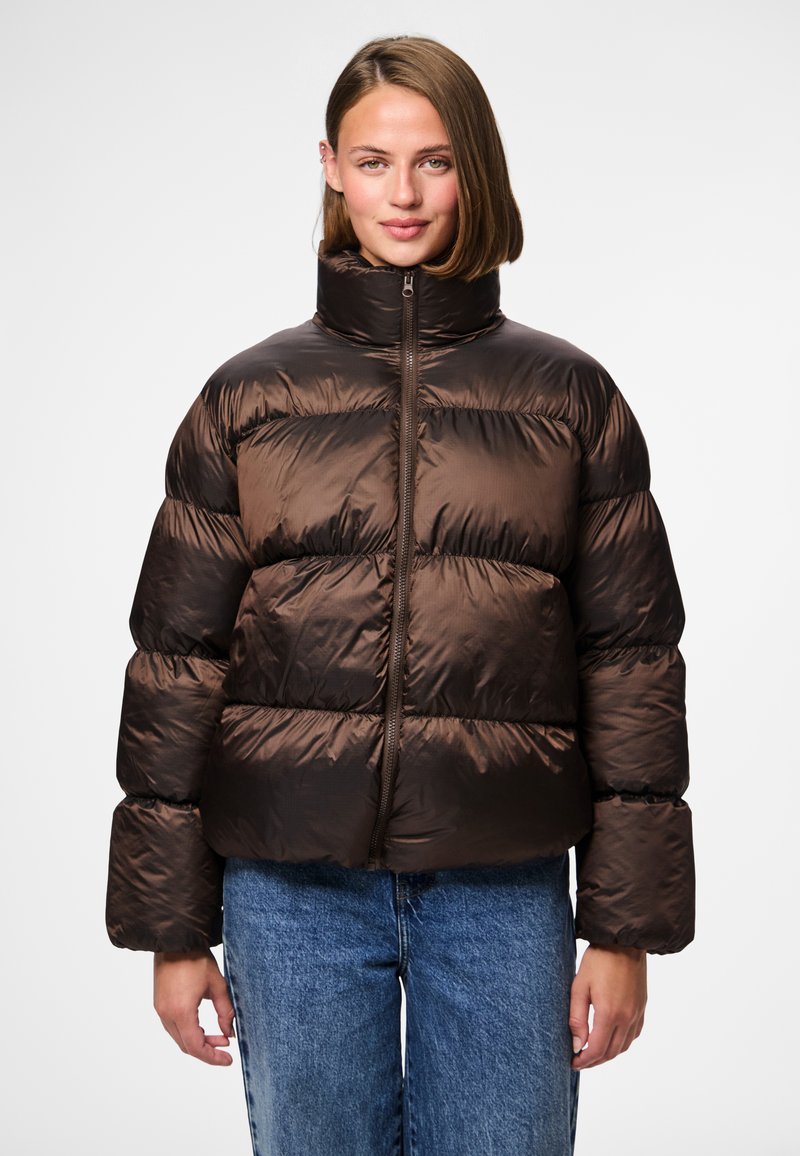 Brun puffjacka med hög krage, texturerat tyg, ribbade muddar och en central dragkedja, kombinerad med blå denimjeans.