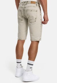 Lys beige denimshorts med en let slidt finish, i midt-lår længde, fem lommer og en læder rygpatch. Stylet med hvide sneakers.