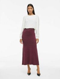 Bílý top s dlouhým rukávem z texturované látky, spárovaný s bordo pletenou maxi sukni. Černé lodičky s špičatou špičkou doplňují outfit.