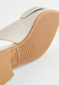 Vaaleanbeige sandaalit, joissa on sileä keinonahkainen päällinen, avoin varvaspääty ja teksturoitu tan-värinen kumipohja, jossa on timanttikuviot.
