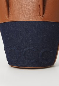 Brown leather and dark blue denim bag with embossed letters "OCC" on the denim section, featuring sturdy handles and a textured finish.