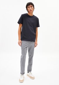 T-shirt en coton bleu marine à col rond associé à un pantalon rayé gris et des baskets blanches avec des accents beiges. Design simple et décontracté.