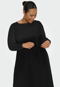 Robe noire à manches longues en tissu doux, dotée d'un col rond et d'un détail à nouer à la taille, offrant une coupe décontractée.