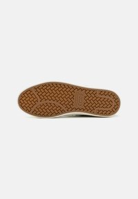 Brown rubber shoe sole with a textured grid pattern, featuring a white midsole and the “Converse” logo embossed near the heel area.