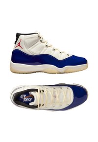 Baskets montantes blanches et bleues avec une tige en cuir lisse, des accents bleus en vernis, une languette blanche texturée et une semelle en caoutchouc. Détail de logo rouge.