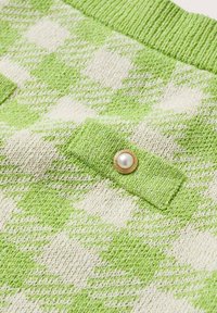 Tessuto a maglia a scacchi verde e bianco con una superficie testurizzata, caratterizzato da un accento con bottone dorato e dettagli in perla.