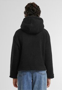 Svart fleecehoodie med mjuk textur, stor huva och sänkta axlar. Bärs tillsammans med ljusblå högmidjade jeans som ger en avslappnad passform.