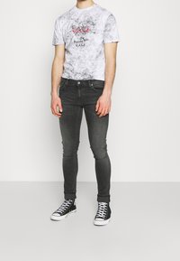 Grå mönstrad t-shirt med röd grafik och svarta tajta jeans, kompletterat med svarta sneakers med högt skaft. Slät tyg och figursydd design.