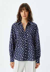 Camisa de botones azul marino con estampado de estrellas blancas, mangas largas, cuello clásico y un corte holgado. Tejido suave y ligero.