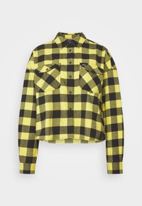 Camicia di flanella a quadri gialli e neri, tagliata. Maniche lunghe, chiusura con bottoni sul davanti e due tasche sul petto con pattine. Texture morbida.