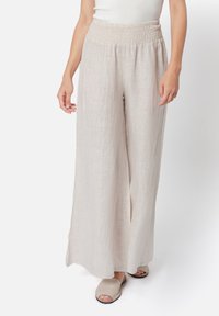 Pantaloni ampi, leggeri e beige con una vita arricchita e una sottile texture, abbinati a semplici sandali beige a ciabatta.