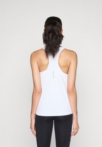 Canottiera atletica bianca senza maniche, design a schiena scoperta, con una linea verticale di piccoli punti sulla schiena, abbinata a leggings neri.