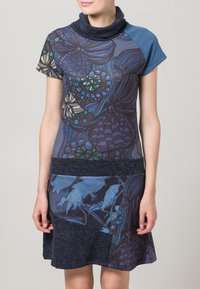 Robe à manches courtes avec un col bénitier, présentant des sections bleues et sombres à motifs, et une ceinture texturée sombre avec des accents floraux.