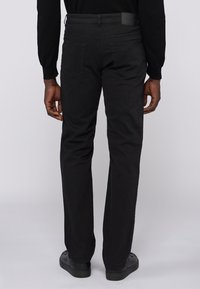 Pantalones rectos negros hechos de una mezcla de algodón, con bolsillos traseros y un parche de cuero en la cinturilla.