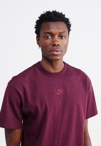 Maroon Nike t-paita, joka on valmistettu puuvillasta, jossa on pyöreä pääntie, lyhyet hihat ja pieni logo rinnassa. Pehmeä rakenne ja rento istuvuus.