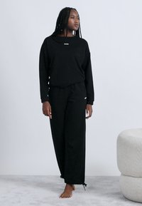 Musta collegepaita ja vastaavat collegehousut, joissa rento istuvuus, yksinkertainen rintalogo ja kiristysnauhat hihansuiden kohdalla.