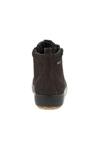 Dunkelbrauner Wildleder-Ankle-Boot mit einem strukturierten grauen Innenfutter, flacher Gummisohle und einer kleinen Lasche an der Rückseite für ein einfaches Anziehen.